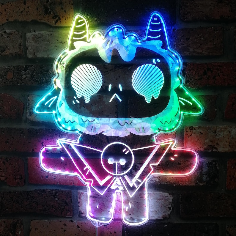 May include: A neon sign depicting a cartoon character with a dark face, large eyes, and horns. The sign is illuminated with a spectrum of colours, including blue, green, and pink. The sign is mounted on a brick wall.