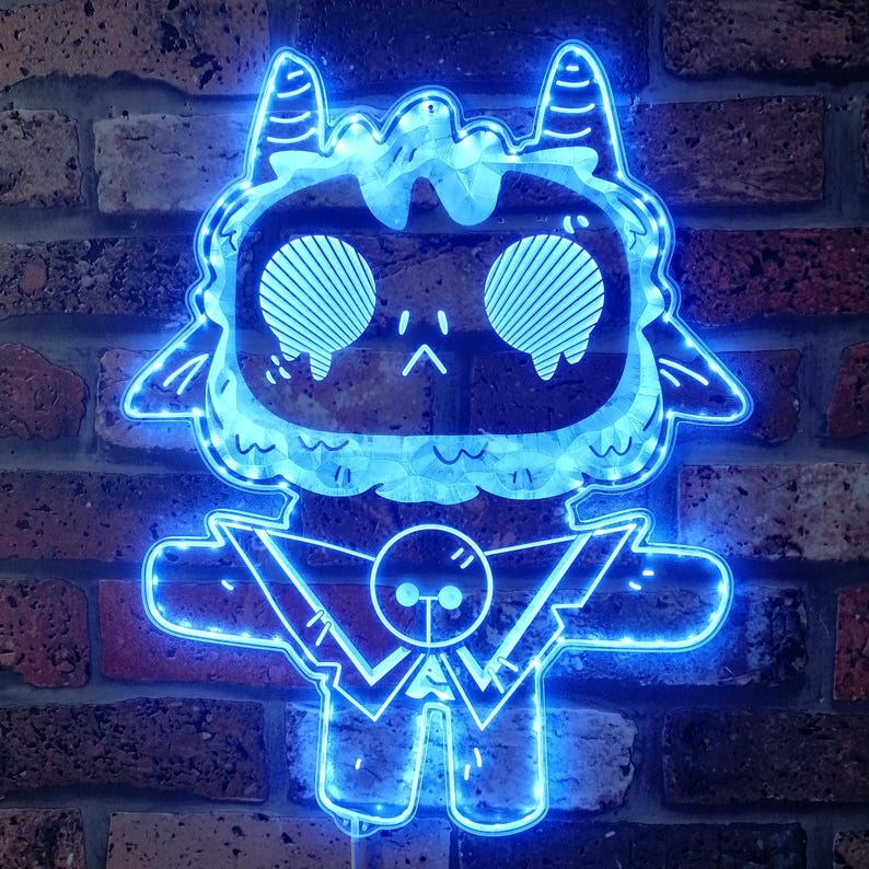 May include: A blue neon light in the shape of a cartoon creature with large eyes, horns, and outstretched arms. The light is mounted on a brick wall, creating a contrast between the modern design and the rustic background.