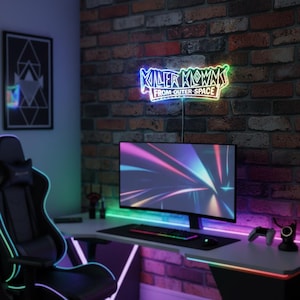 Könnte beinhalten: Ein Gaming-Setup mit einem Neonschild mit der Aufschrift "Killer Klowns From Outer Space". Der Schreibtisch hat einen Monitor, eine Tastatur, eine Maus und einen Controller. Der Stuhl und der Schreibtisch haben LED-Leuchten. Der Hintergrund ist eine Backsteinmauer.