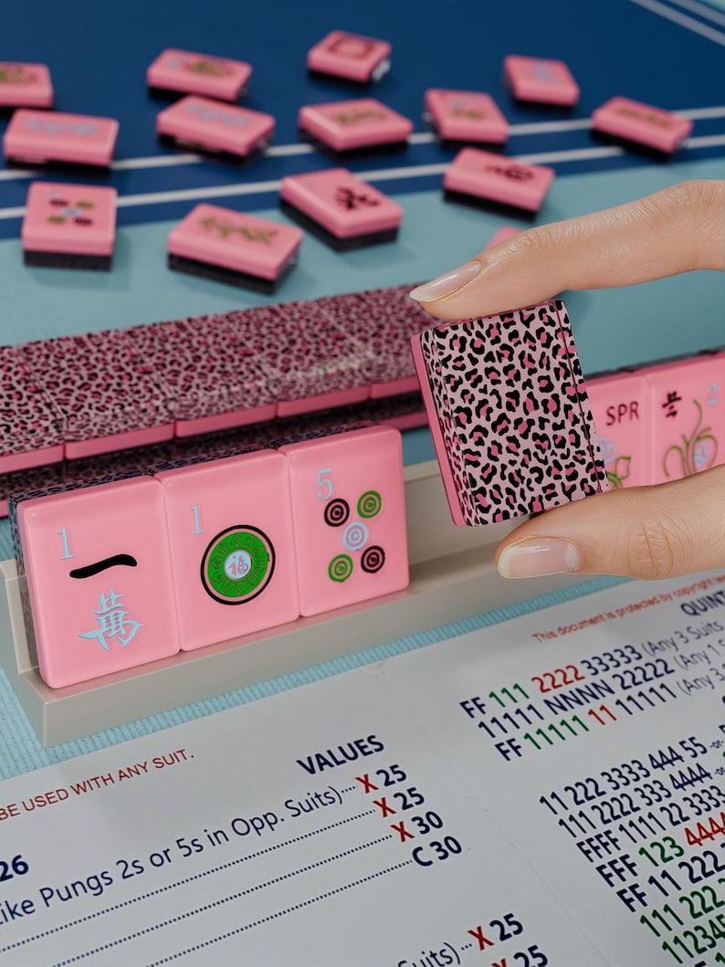 A hand is holding a pink pumkin with a leopard print pattern, with a pink and blue background featuring a game board and tiles.