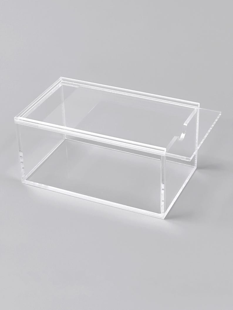 A clear, rectangular, and transparent plastic box with a handle on the right side.