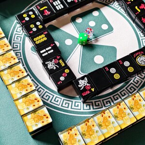 A domino game set up on a green table, with multiple dominoes arranged in a pattern and a single green die placed in the center.