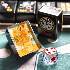 a playing card with a sunflower design, a glass dice, and a deck of playing cards on a table.