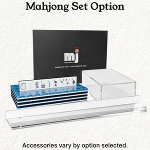 a set of Mah Jongg tiles and accessories, including a black box with the Mah Jongg logo and text, a stack of blue tiles, and a clear plastic case. The text above the image reads "Mahjong Set Option" and below the image, it states "Accessories vary by option selected."