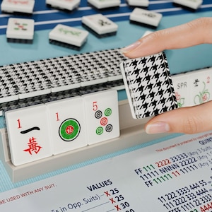 A hand is holding a black and white houndstooth tile in front of a table with a blue surface and a stack of tiles.