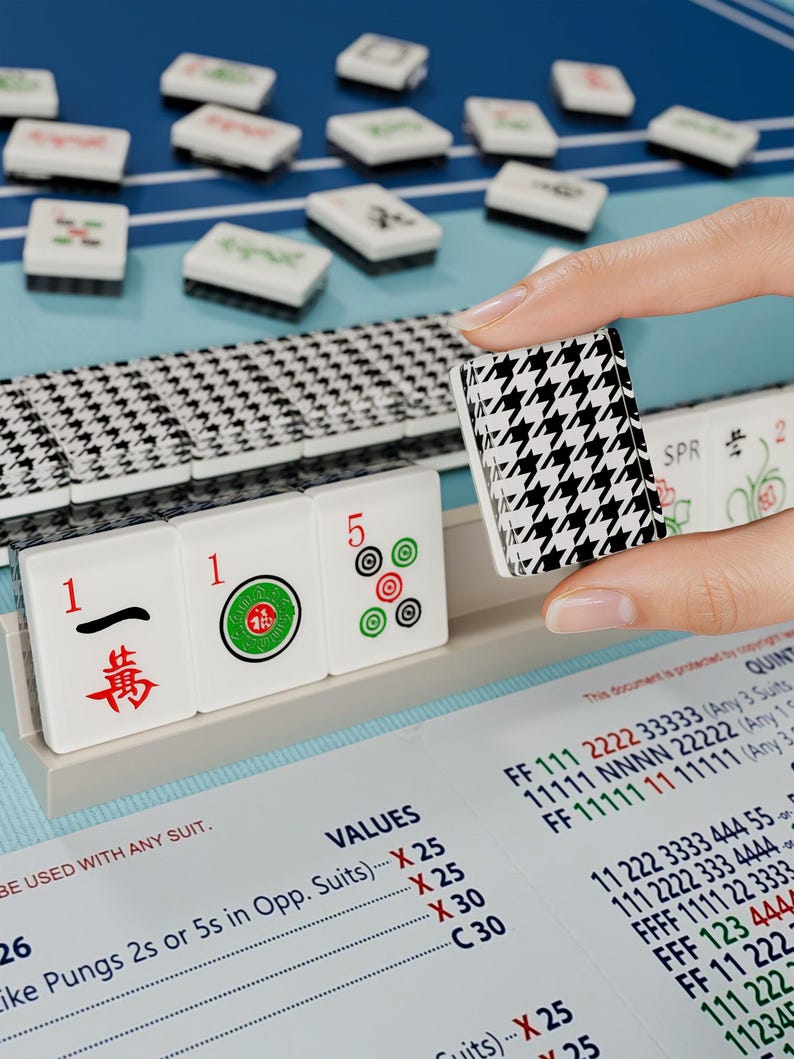 A hand is holding a black and white houndstooth tile in front of a table with a blue surface and a stack of tiles.