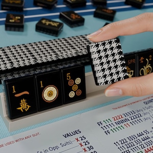 A hand is holding a small black and white houndstooth-patterned object, which appears to be a game piece, in front of a collection of similar-looking game pieces on a blue surface.