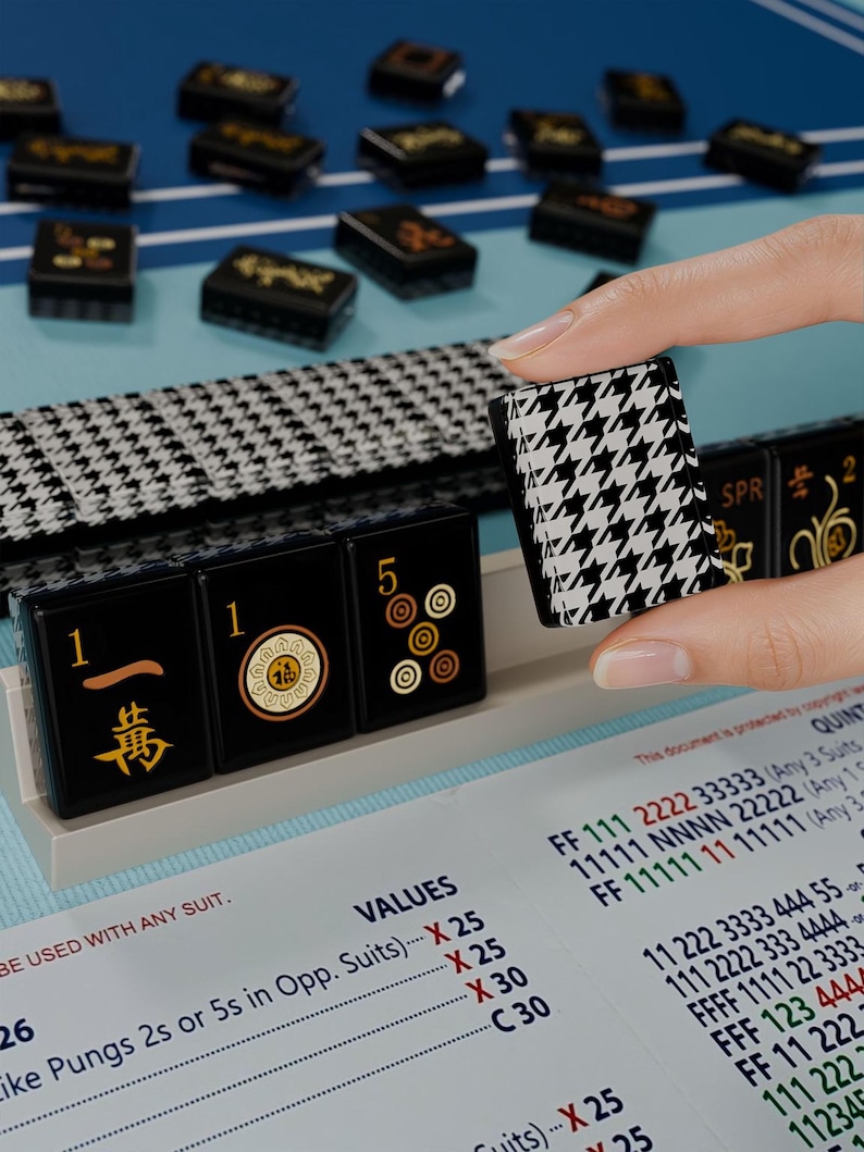 A hand is holding a small black and white houndstooth-patterned object, which appears to be a game piece, in front of a collection of similar-looking game pieces on a blue surface.