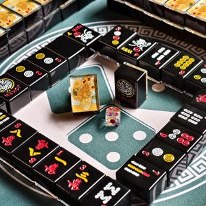 a collection of black and yellow tiles arranged in a grid-like pattern, with some of the tiles featuring Chinese characters. There are also two dice and a small figurine on the surface, suggesting a game of mahjong or a similar tile-based game.