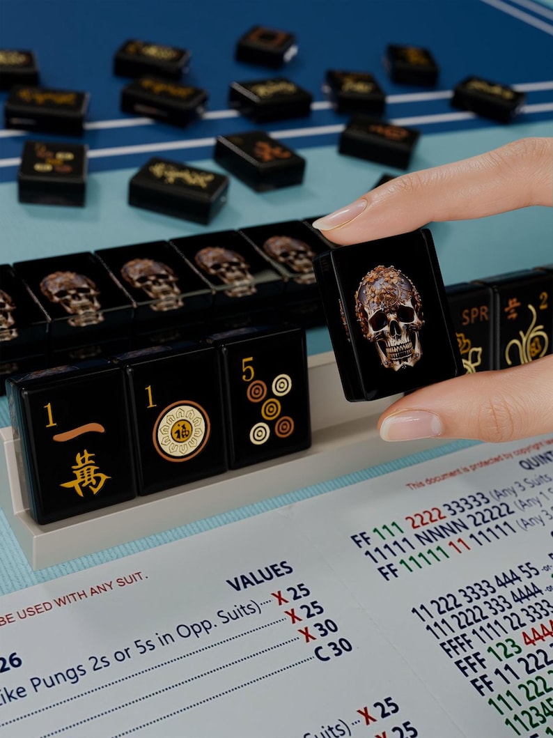 A hand is holding a black game piece with a skull design, while a table with a blue surface displays a list of game pieces and their values.