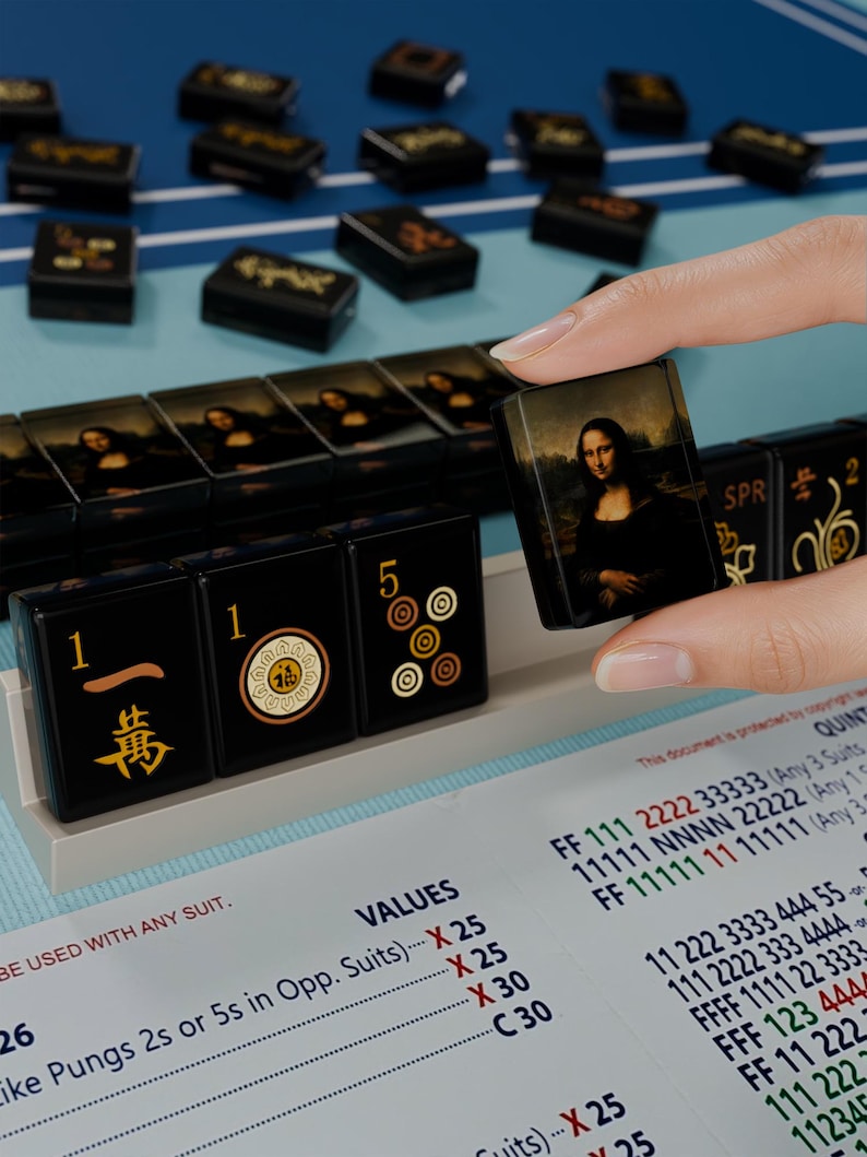 A hand is holding a small square with a picture of the Mona Lisa on it, in front of a collection of black and gold dominoes.