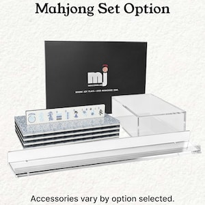 a set of Mah Jong tiles and a black box with the text "Mahjong Set Option" on it. The text indicates that the set is available in various options, and the image shows a clear plastic shelf with the tiles and a black box with the same text.