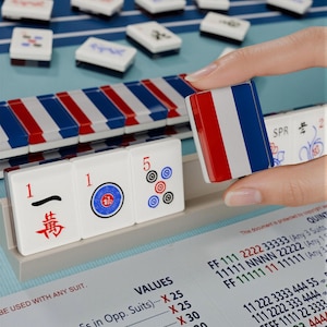 A hand is holding a red, white, and blue tile in front of a table with a blue and white checkered pattern.