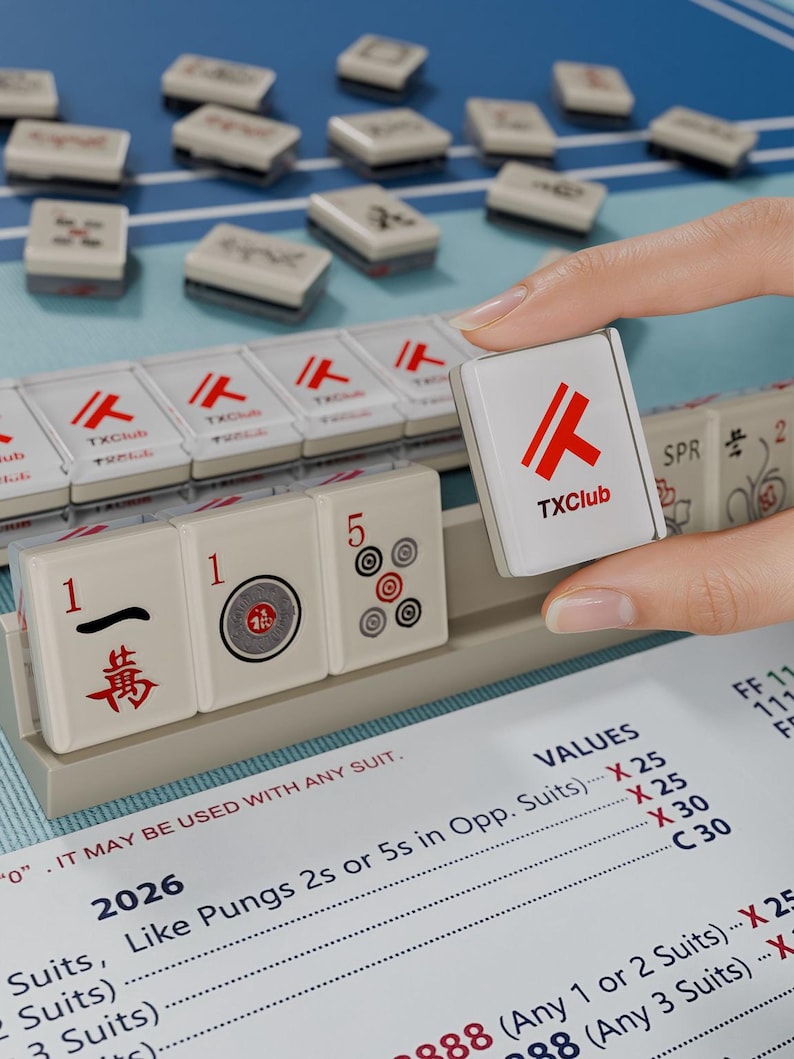 A hand is holding a tile with the TX Club logo, while a game of mahjong is visible in the background.