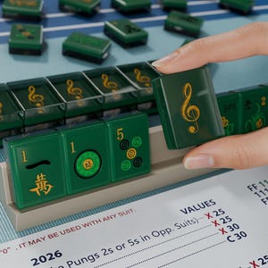 A hand is holding a green tile with a musical note symbol on it, in front of a collection of green tiles on a blue surface.