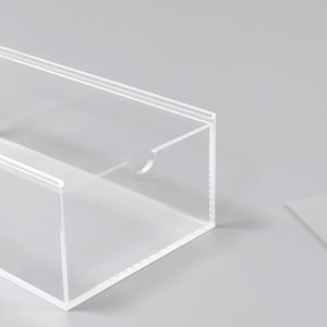 A transparent, clear plastic box with a cutout on the side, sitting on a plain white surface.