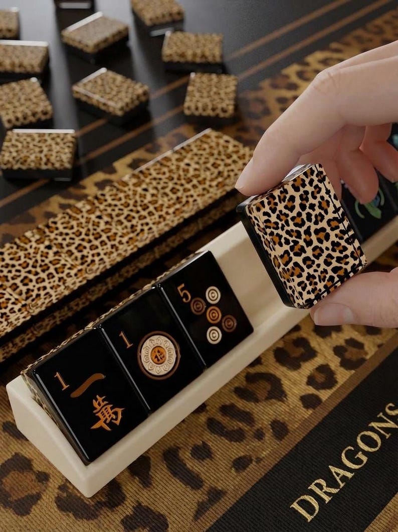 A hand is holding a leopard print tile in front of a set of black and white tiles with Chinese characters, arranged on a leopard print surface.