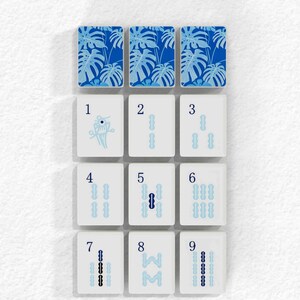 nine tiles, each with a different pattern or design, arranged in a grid-like pattern. The tiles are white and feature various patterns, such as palm leaves, flowers, and abstract shapes. The tiles are arranged in a visually appealing manner, showcasing the diversity and creativity of the designs.