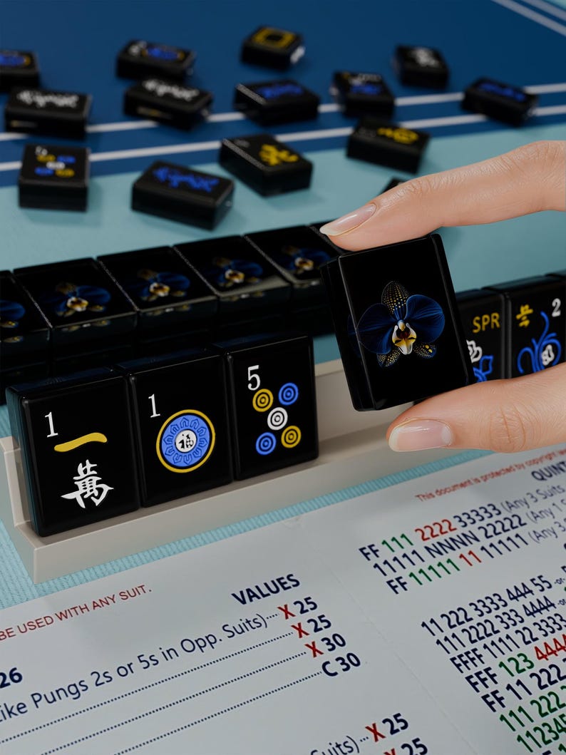 A hand is holding a black game piece with a blue and yellow design, standing in front of a table with a blue and white checkered pattern.