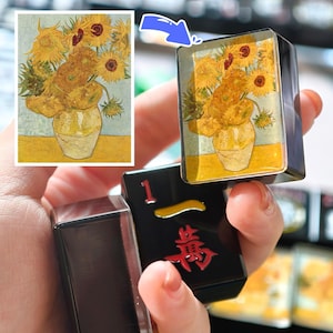 A hand holding a small black object with a Chinese character on it, and a picture of a vase with flowers on it.