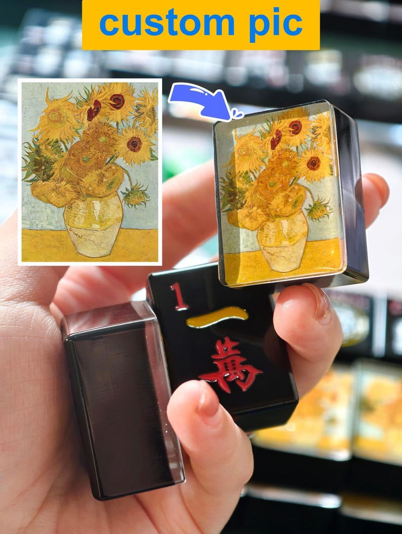 A hand holding a small black object with a Chinese character on it, and a picture of a vase with flowers on it.