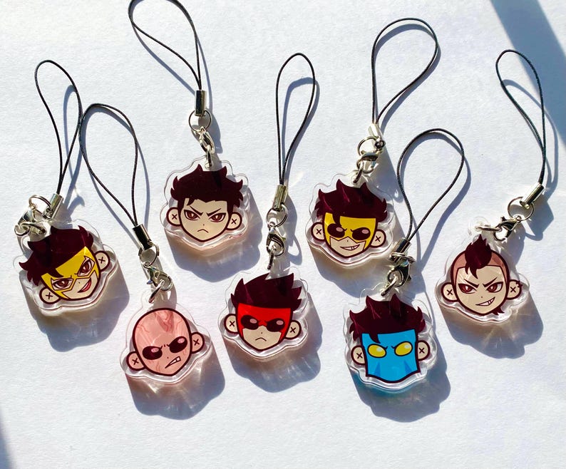 Puede incluir: Colecci&oacute;n de siete colgantes acr&iacute;licos con caras de personajes de dibujos animados con varios colores de pelo y dise&ntilde;os de m&aacute;scaras. Cada colgante est&aacute; unido a un cord&oacute;n negro con un cierre plateado. Las caras tienen diferentes expresiones.