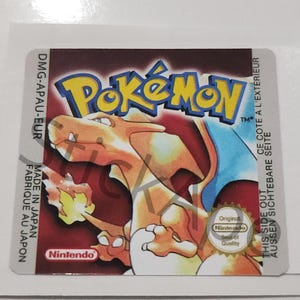 以下が含まれることがあります： ポケモンビデオゲームの長方形ステッカー。ポケモンリザードンが描かれています。ステッカーは赤色の背景に、黄と青のポケモンロゴがあります。任天堂のロゴとテキストも表示されています。