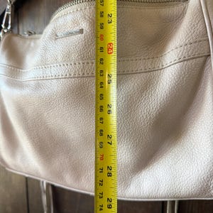 Peut inclure: Un sac &agrave; main en cuir beige clair avec une bandouli&egrave;re en cha&icirc;ne argent&eacute;e. Le sac mesure environ 61 cm de hauteur. Le sac a une fermeture &eacute;clair et des glands d&eacute;coratifs.