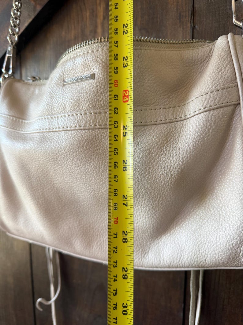 Peut inclure: Un sac &agrave; main en cuir beige clair avec une bandouli&egrave;re en cha&icirc;ne argent&eacute;e. Le sac mesure environ 61 cm de hauteur. Le sac a une fermeture &eacute;clair et des glands d&eacute;coratifs.