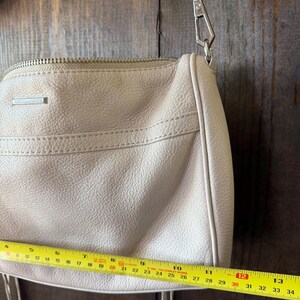 Peut inclure: Un sac &agrave; bandouli&egrave;re en cuir beige clair avec une cha&icirc;ne argent&eacute;e. Le sac a une fermeture &eacute;clair et un petit logo rectangulaire. Le sac mesure environ 30 cm de long.