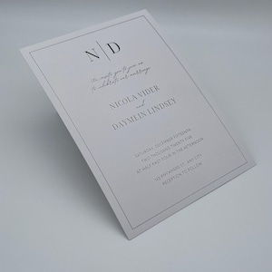 Può includere: Un invito di nozze bianco con un design minimalista. L'invito presenta le iniziali "N D" in alto, seguite dai nomi Nicola Vider e Daymein Lindsey. La data, l'ora e il luogo sono stampati anche sull'invito.