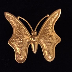 May include: A gold-toned butterfly brooch with intricate filigree details. The butterfly has a rounded body and delicate wings.