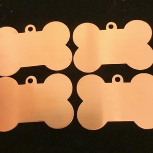 May include: Four blank, copper-coloured dog bone-shaped tags with a hole at the top for attaching a ring or chain.