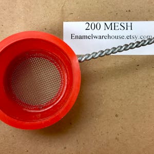 May include: A red, round, plastic strainer with a 200 mesh metal screen. The strainer is used for enamelware and is available on Etsy.