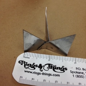 Puede incluir: Un objeto de metal plateado con forma de estrella de cuatro puntas con una regla que mide 3,8 cm de largo.