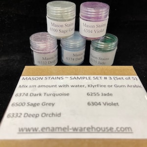 May include: A set of five small jars of Mason Stains in various colors, including sage grey, violet, dark turquoise, deep orchid, and jade. The jars are labeled with the color name and number. The text on the box reads "MASON STAINS SAMPLE SET #3 (Set of 5)" and "Mix sm amount with water, KlyrFire or Gum Arabic".