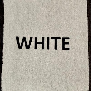Op de afbeelding: Wit vierkant tapijt met het woord "WHITE" in het zwart gedrukt.