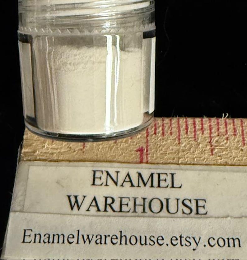 Op de afbeelding: Een klein, helder glazen potje gevuld met een fijn, gebroken wit poeder. Het potje staat op een houten liniaal met rode markeringen. De tekst "ENAMEL WAREHOUSE" en de Etsy shop URL zijn zichtbaar.