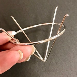 May include: A silver metal cone-shaped stand with a circular base. The stand is made of thin wire and has a delicate design.