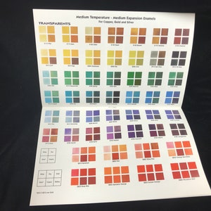 Puede incluir: Una carta de colores para esmaltes de temperatura media y expansión media para cobre, oro y plata. La carta muestra una variedad de colores de esmalte transparente en pequeñas muestras cuadradas. Los colores van desde amarillos y verdes hasta azules y rojos.