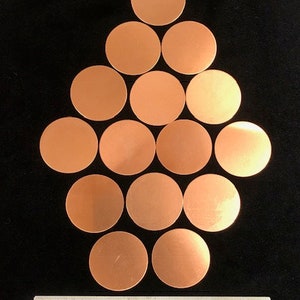 May include: A collection of 15 copper discs arranged in a pyramid shape on a black surface. The discs are all the same size and have a smooth, shiny finish.