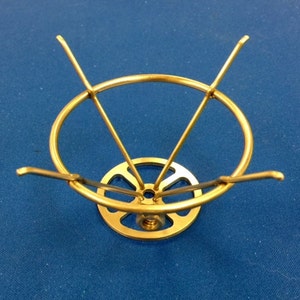 May include: A gold metal stand with a round top and three legs. The stand has a decorative design on the base.