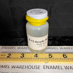May include: A clear plastic bottle of A-13 Acrylic Medium (Water Base) with a white label and a yellow cap. The bottle contains 2 fl. oz. of liquid. A ruler is placed in front of the bottle.