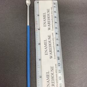 May include: A silver metal spoon with a blue handle, measuring approximately 4 inches in length. The spoon is used for applying enamel to crafts.