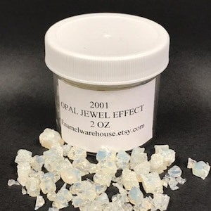 May include: A clear jar filled with small, white, iridescent opal pieces. The jar has a white lid and a label that reads "2001 Opal Jewel Effect 2 oz Enamelwarehouse.etsy.com".