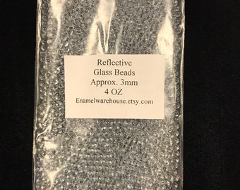 May include: A clear plastic bag filled with small, reflective, clear glass beads. The bag has a label that reads "Reflective Glass Beads Approx. 3mm 4 OZ Enamelwarehouse.etsy.com".