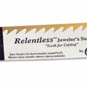 Peut inclure: Un paquet de lames de scie à chantourner Relentless "Golden Extra" de fabrication suisse, étiqueté "Teeth for Cutting" et "Superior Quality". L'emballage est doré et blanc avec un drapeau suisse rouge.