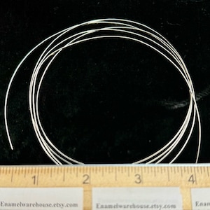 May include: A close-up of silver wire, coiled into a circle, measured against a ruler. The wire is approximately 3 inches in diameter.