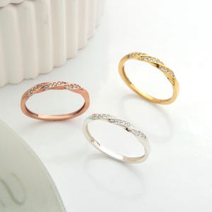 Könnte beinhalten: Drei zarte Ringe in Roségold, Gold und Silber, jeweils mit einer Reihe kleiner, funkelnder Steine. Die Ringe werden auf einer weißen Oberfläche präsentiert, mit einer weißen dekorativen Box und einem Band im Hintergrund.