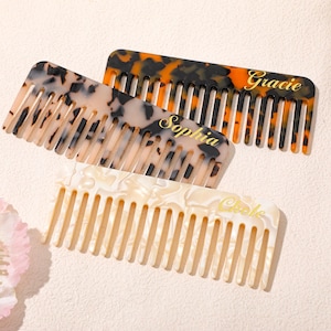 Op de afbeelding: Drie gepersonaliseerde kammen in schildpad-, crème- en marmerpatronen. De kammen zijn gegraveerd met de namen "Gracie", "Sophia" en "Chloe" in gouden letters. De kammen zijn gerangschikt op een lichtgekleurd oppervlak.
